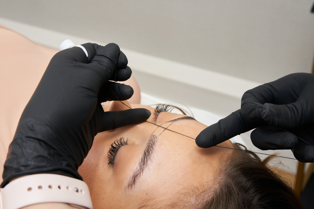 A woman's face with her eyebrows being shaped and tinted by a brow artist at Brow HQ.